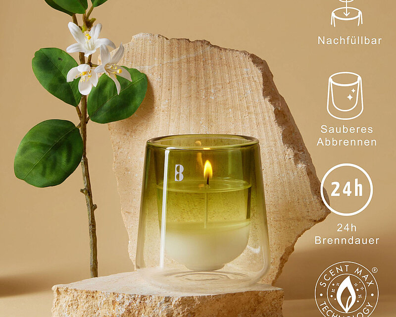 Das Bild zeigt ein stilvoll inszeniertes Bolsius CleanLight Duftglas in einem modernen, natürlichen Ambiente. Die grüne Duftkerze ist in einem hochwertigen, doppelwandigen Glasgefäß platziert und steht auf einem hellen Naturstein, begleitet von einer zarten Blüte mit grünen Blättern. Umgeben von natürlichen Elementen vermittelt das Bild Ruhe, Reinheit und Nachhaltigkeit. Grafische Icons heben die Vorteile des Produkts hervor: nachfüllbar, sauberes Abbrennen, 24 Stunden Brenndauer und Scent Max® Technologie für maximale Duftfreisetzung.
