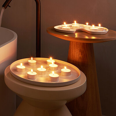 Warme Wellnessstimmung im Badezimmer mit brennenden Teelichtern und großzügigen Maxi-Teelichtern – platziert auf Holzablagen um Wanne und Becken für stimmungsvolle Lichtakzente.